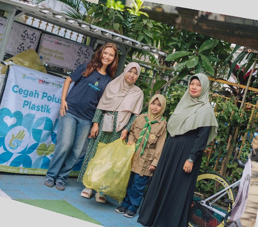 A family standing beside a Plastic Bank collection cart branded Cegah Polusi Plastik
