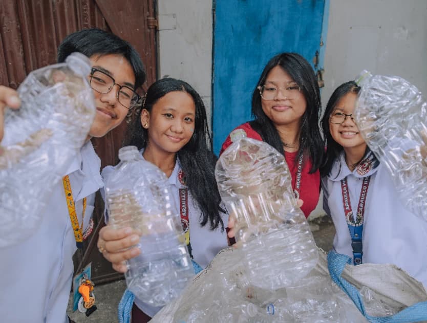 Four students holding up used plastic bottles they have brought in to recycle