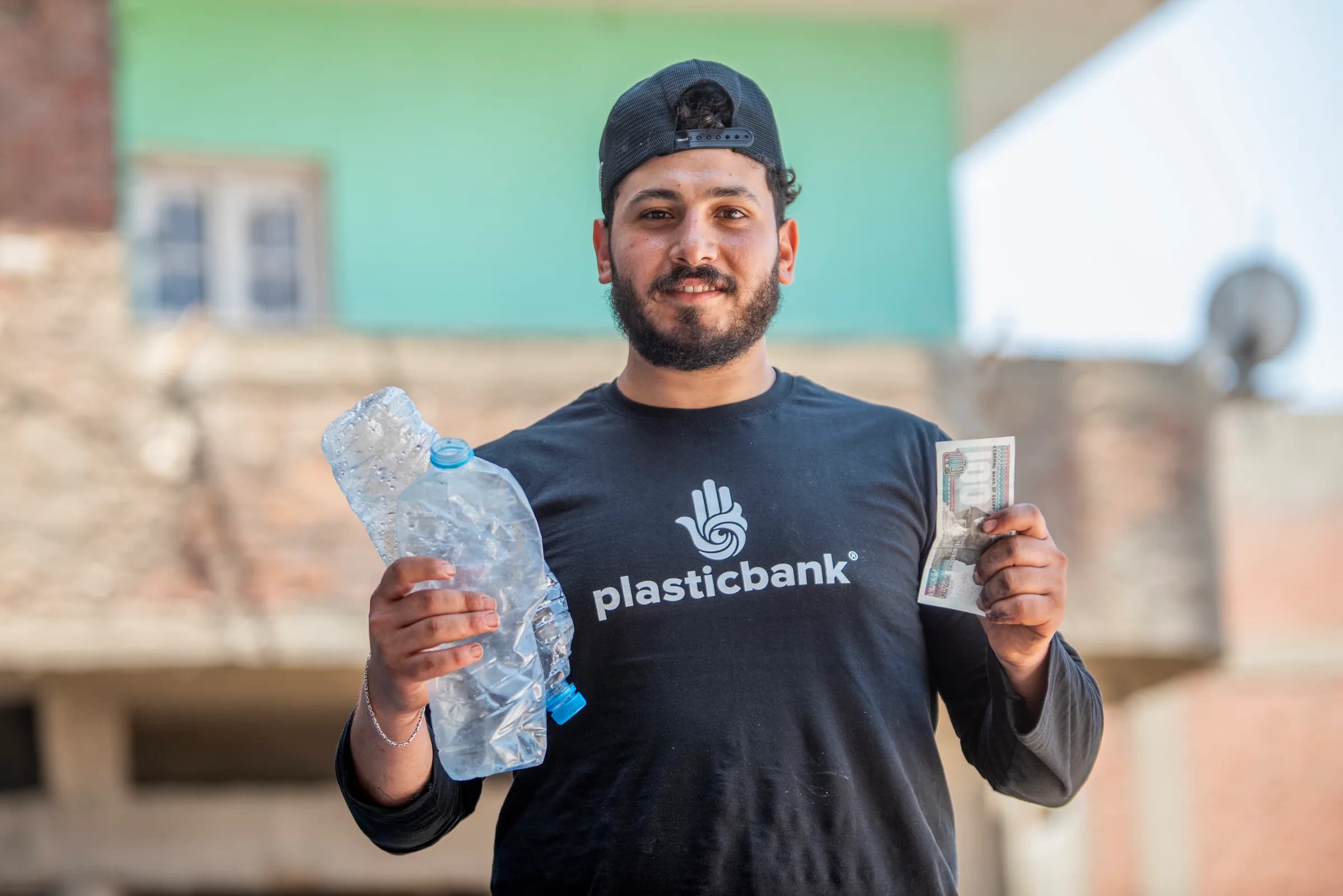 A Plastic Bank collection member in Egypt holding a plastic bottle in one hand and the cash he exchanged it for in the other