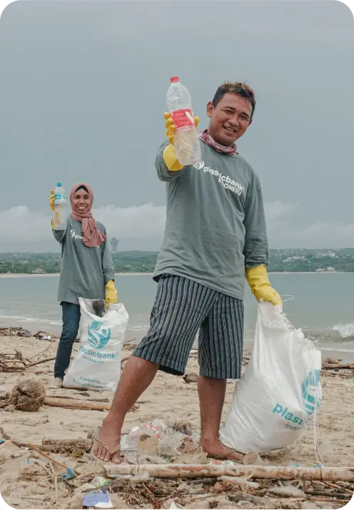 Two community members from Plastic Bank Indonesia gather plastic bottles on Kedonganan Beach. They are smiling and holding up the collected plastic, showcasing their efforts to clean the beach and contribute to reducing plastic pollution.