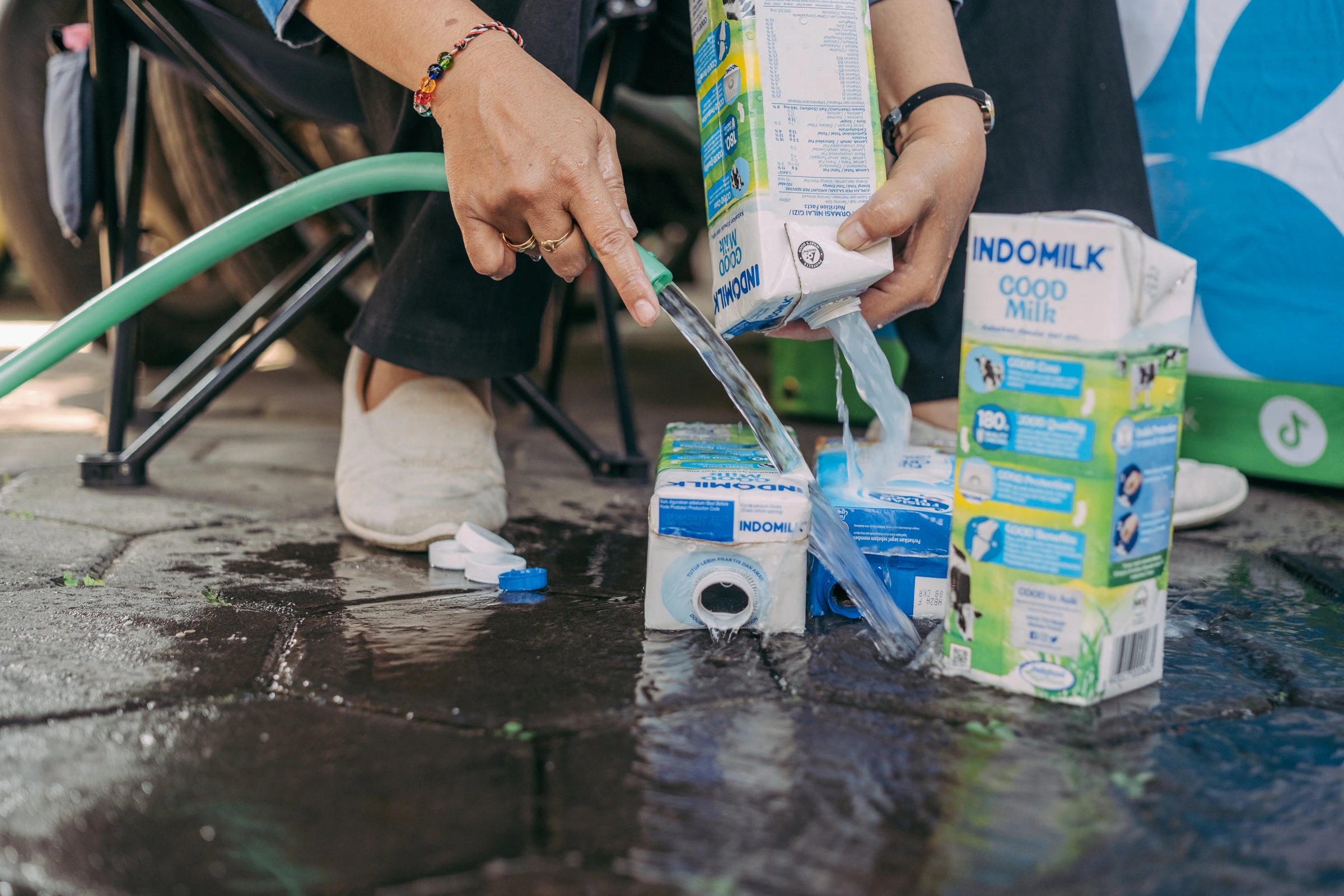 Hands rinsing empty milk cartons with a hose before drop-off