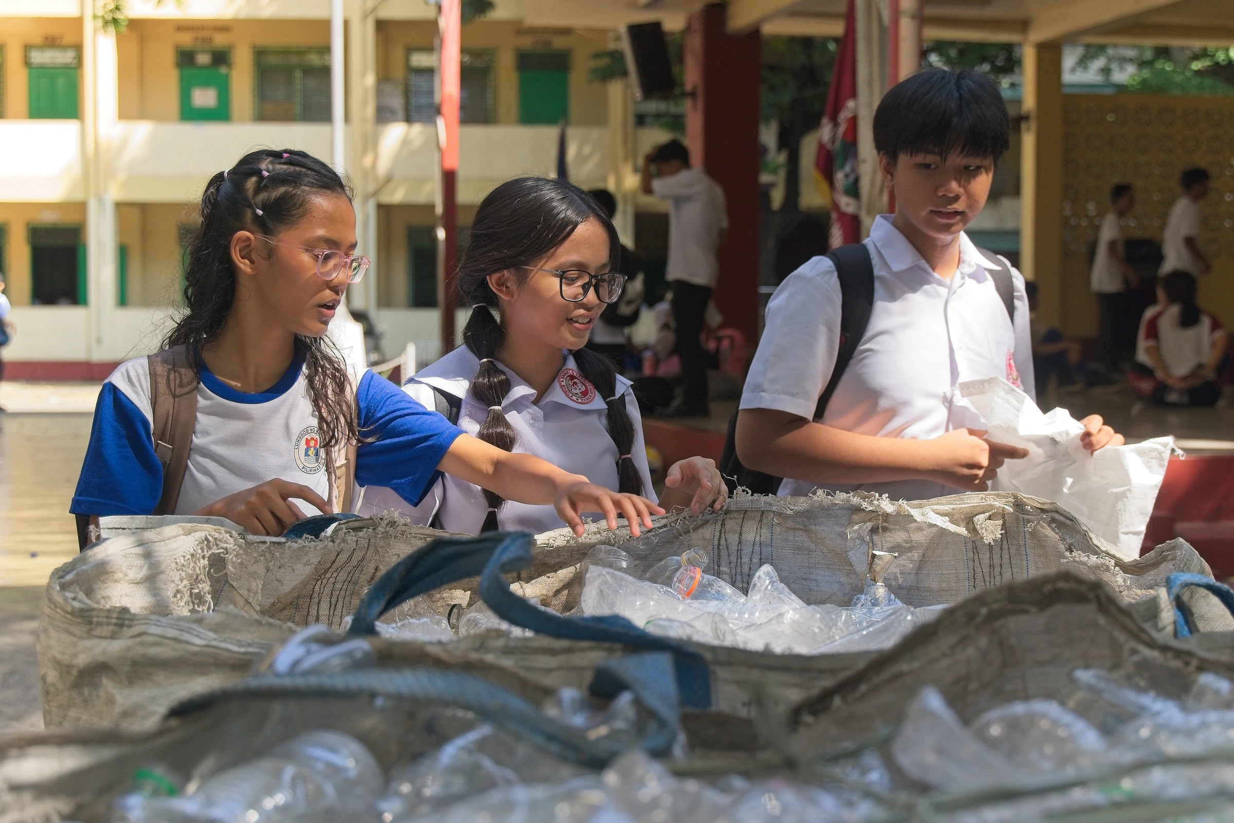 Students dropping plastic bottles into a collection sack at Araullo High School