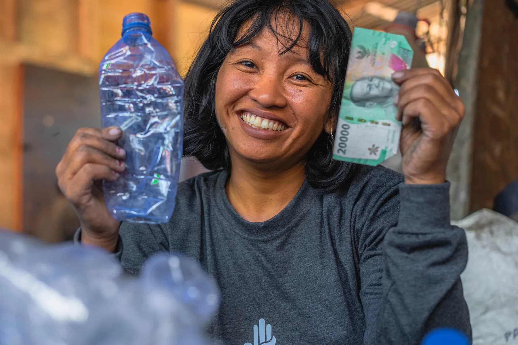 Asnaini, a Plastic Bank collection member in Indonesia, holding a gathered bottle in one hand and the income she was paid for it in the other