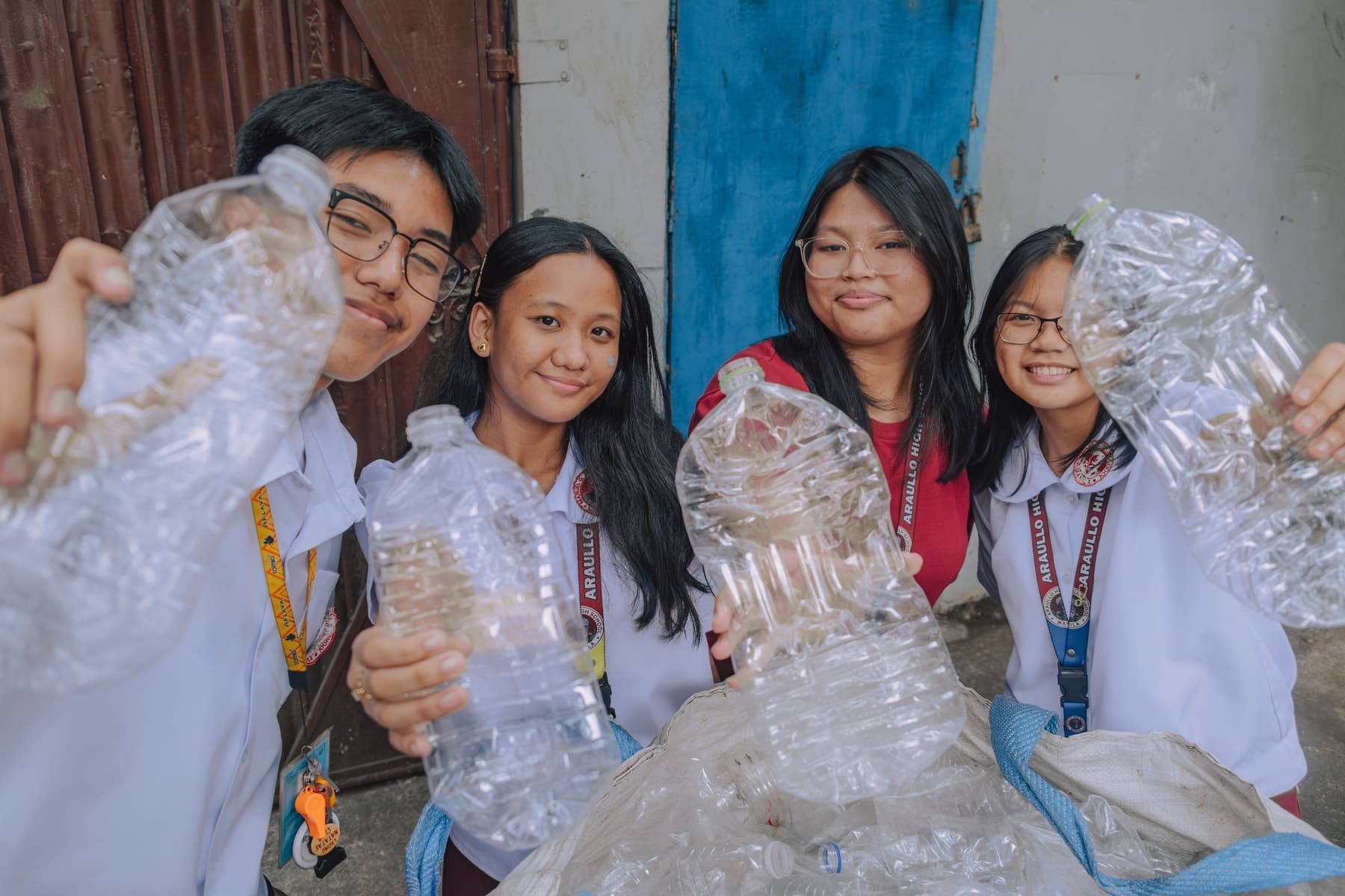 Four students holding up used plastic bottles they have brought in to recycle