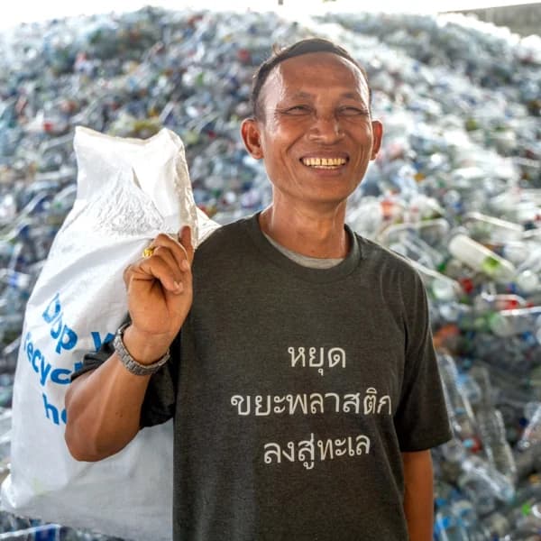 Plastic Bank member Panya holding a collection sack in front of gathered plastic bottles in Thailand