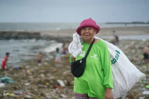 Plastic Bank member carrying a collection sack along a shoreline