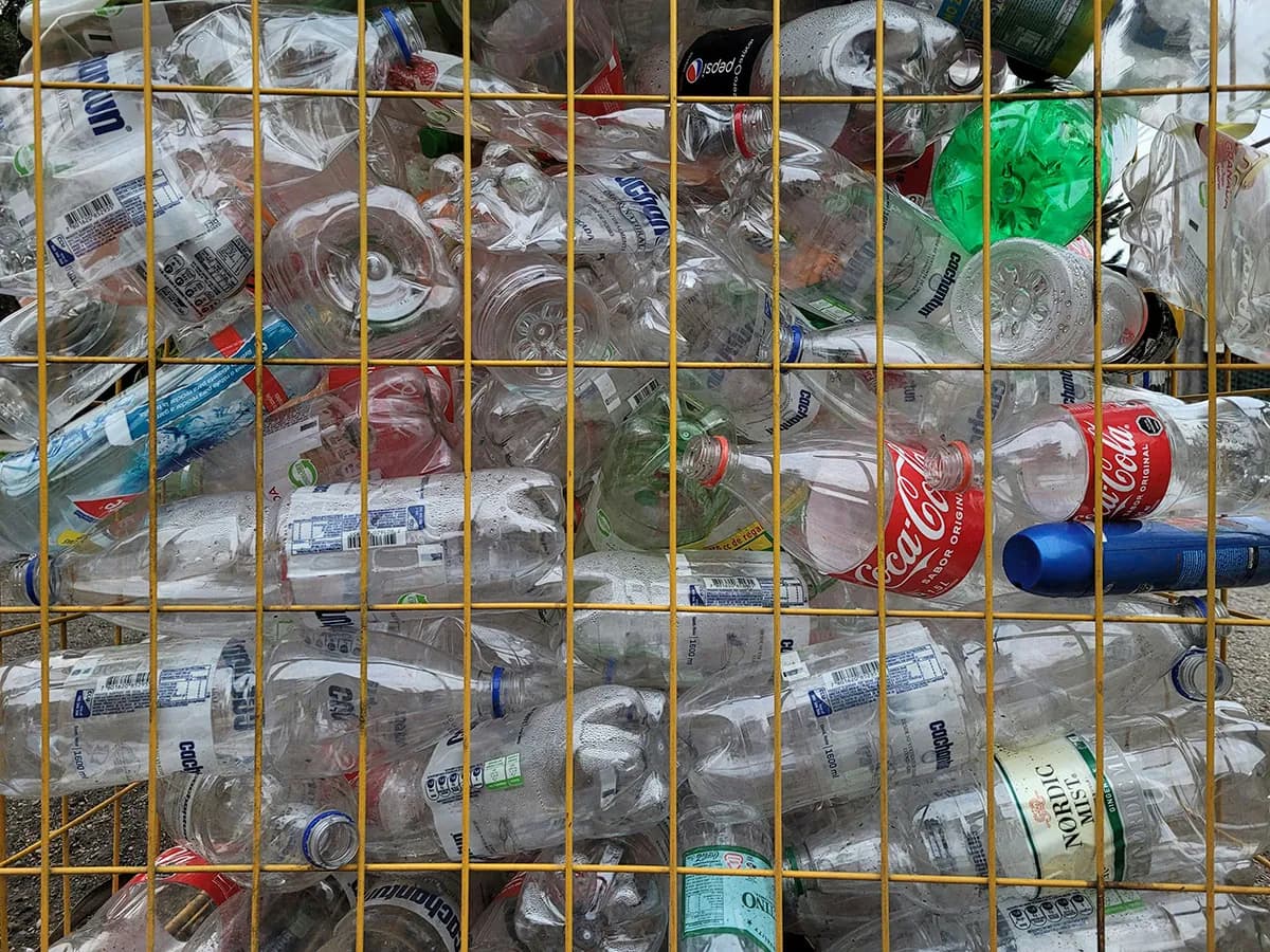 Used plastic bottles and cans packed tightly in a yellow wire basket, ready for recycling.