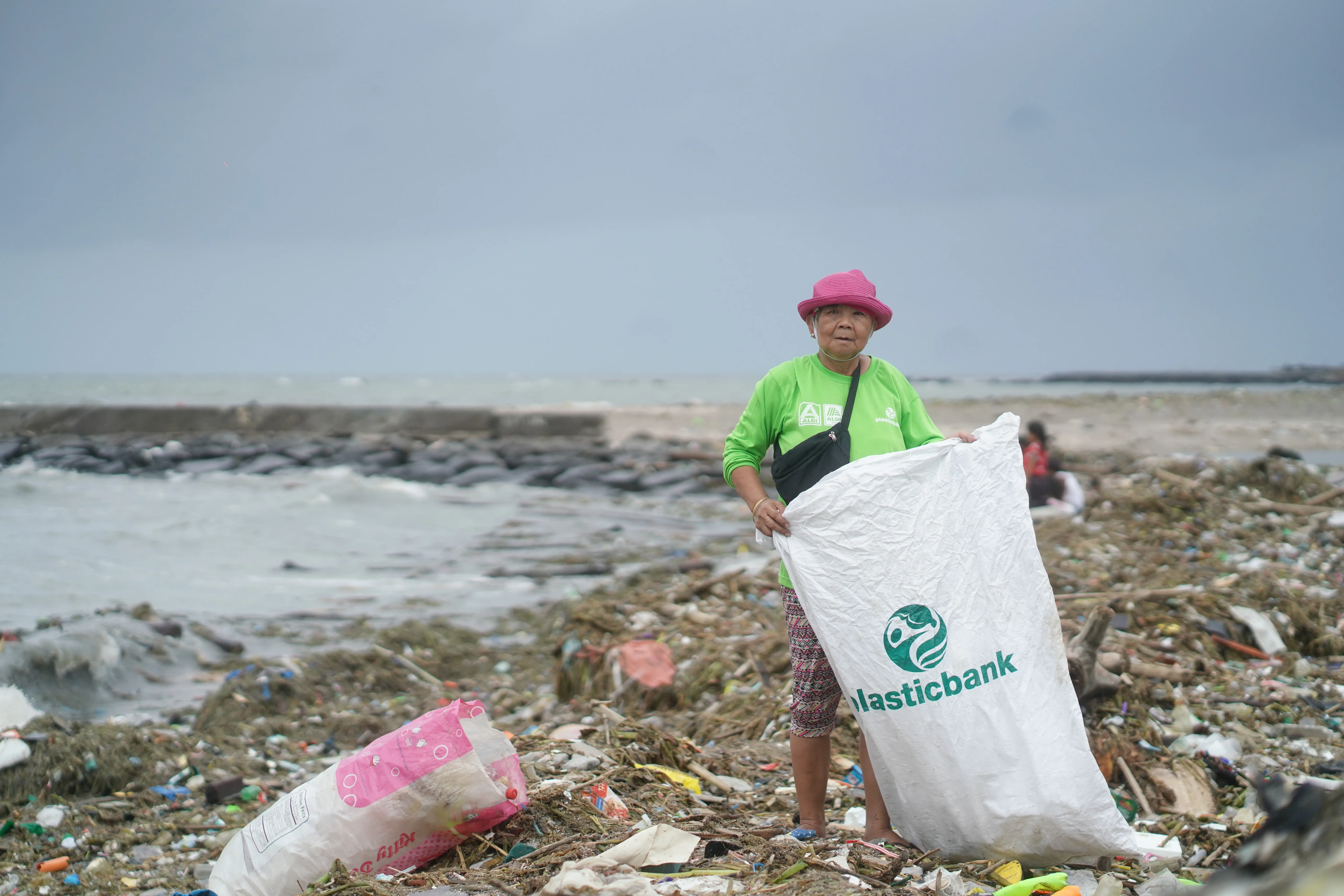 Elizabeth Ampuyas is shown holding a “Plastic Bank” bag on a beach with visible pollution.
